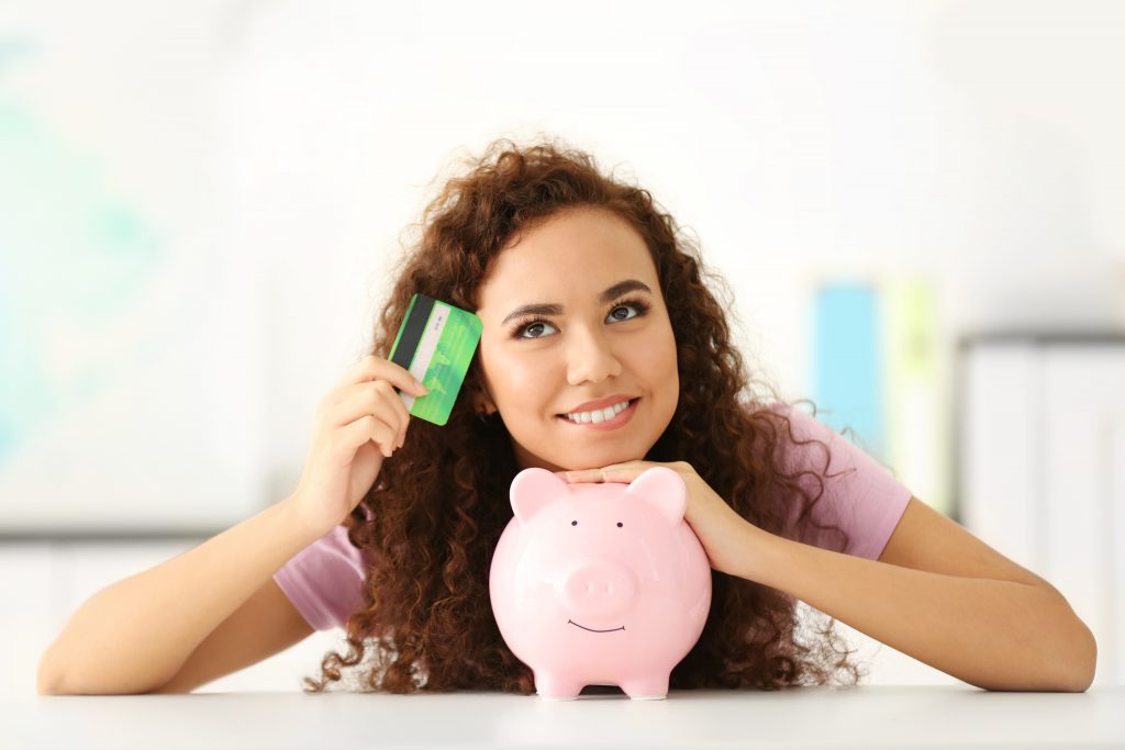 Beautiful young girl with piggy bank and credit card in office.