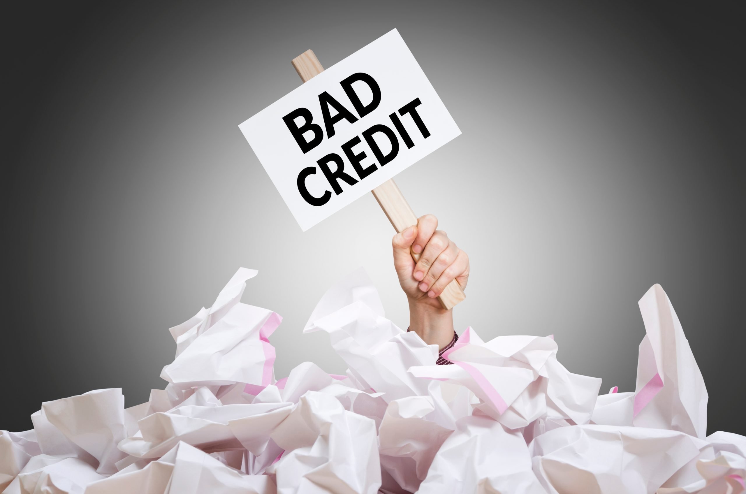 Bad credit placard in hand with crumpled paper pile