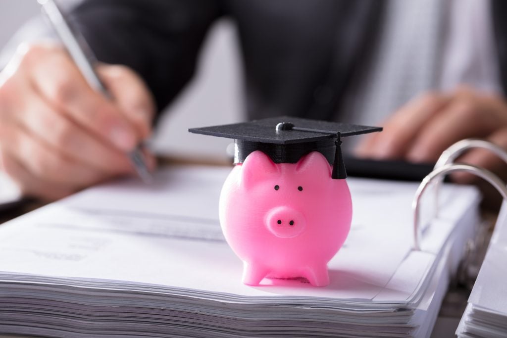 Close-up Of Pink Piggybank With Graduation Cap On Document