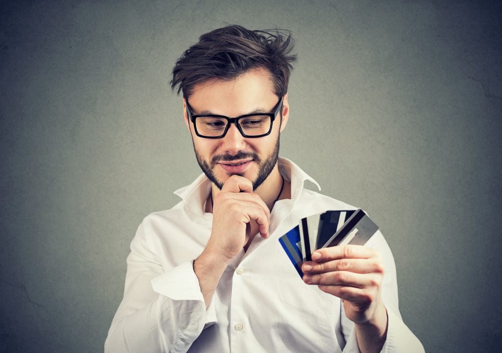 Young handsome man in glasses having choice of credit cards excited with financial stability.