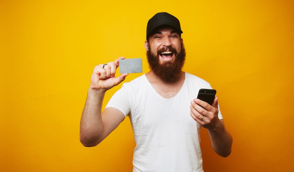 Cheerful man with beard holding credit card and smartphone