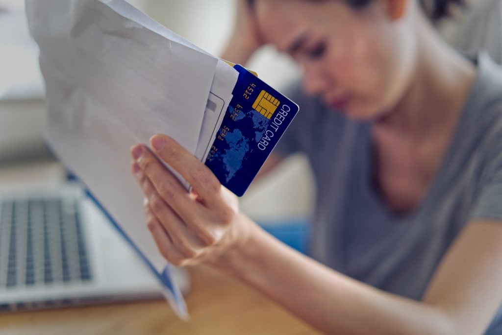 Stressed young sitting Asian woman hands holding credit card and bills worry about find money to pay credit card debt and all loan bills. She is feeling stressful. Financial problem concept.