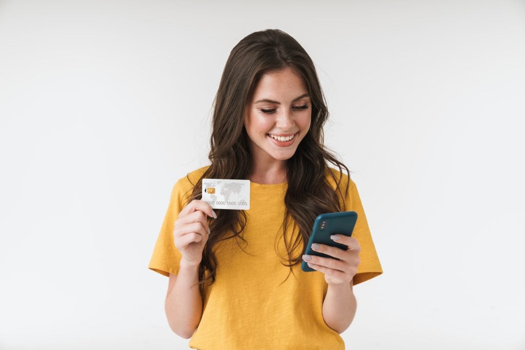 Image of gorgeous brunette woman wearing casual clothes holding credit card and cellphone isolated over white background
