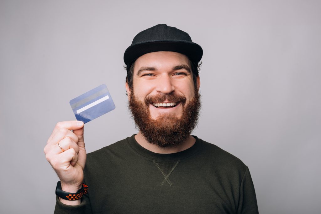 Close up portrait of a smiling bearded man showing a blue credit or debit card on white background.