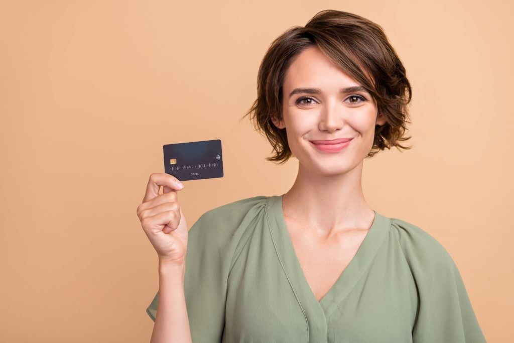 Happy young woman smile holding credit card beige color background