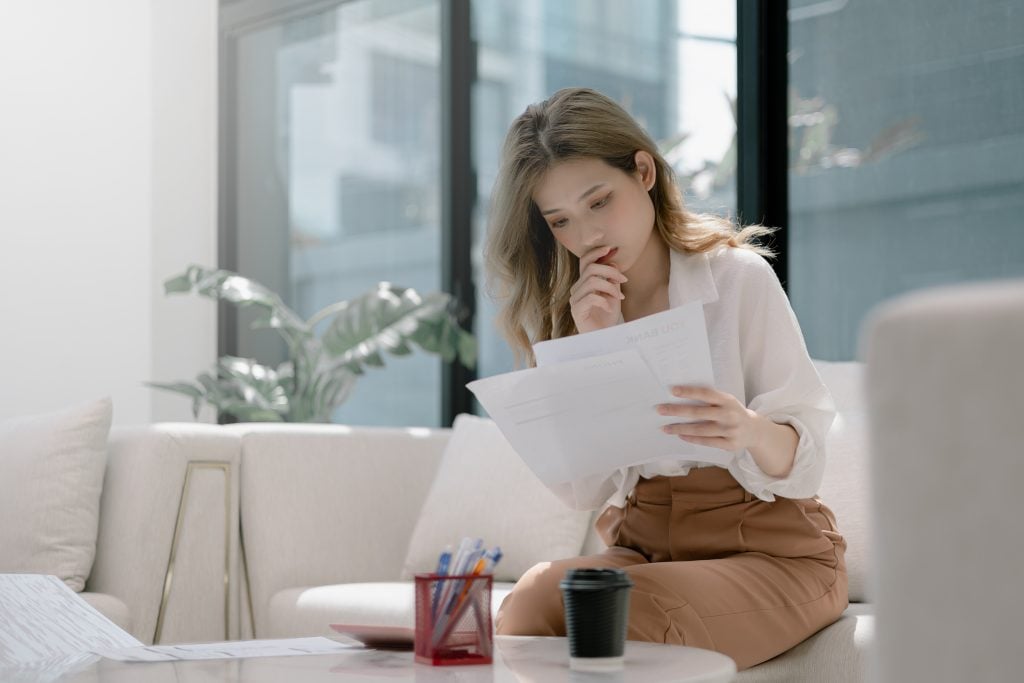 Beautiful young asian woman sitting at living room feeling stressed calculating monthly home expenses, taxes, bank account balance and credit card bills payment, manage budget, accountancy concept.