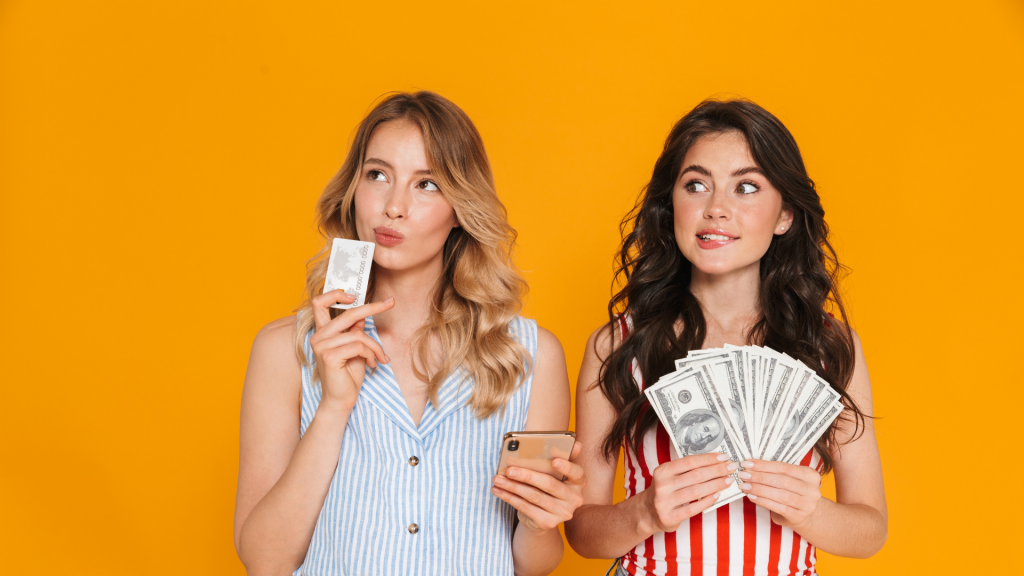 Portrait of thinking nice women 20s in summer wear using cellphone while holding credit card and money bills