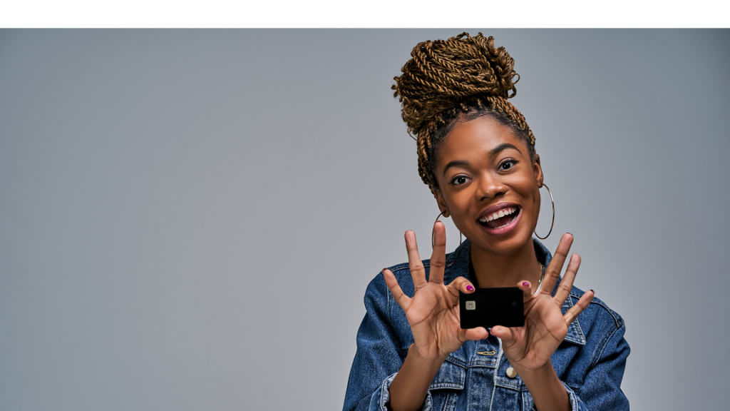 A girl with a smile in a jeans jacket shows a black bank credit card in her hands. Banking concept