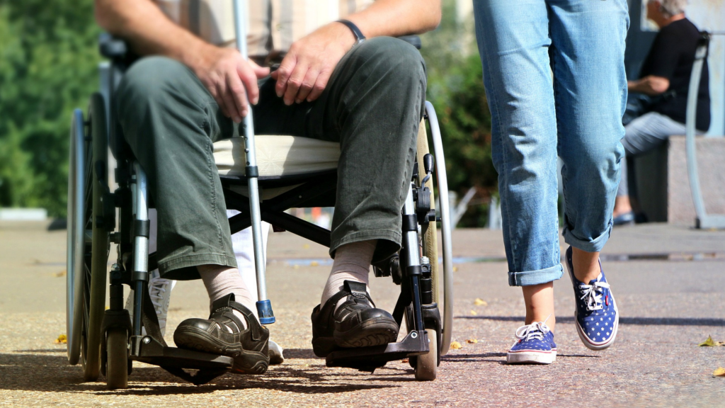 old man in a wheelchair walking side by side with a young woman (focus on both legs)