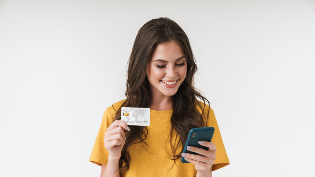 Image of gorgeous brunette woman wearing casual clothes holding credit card and cellphone (apply Mission Lane Visa® card)