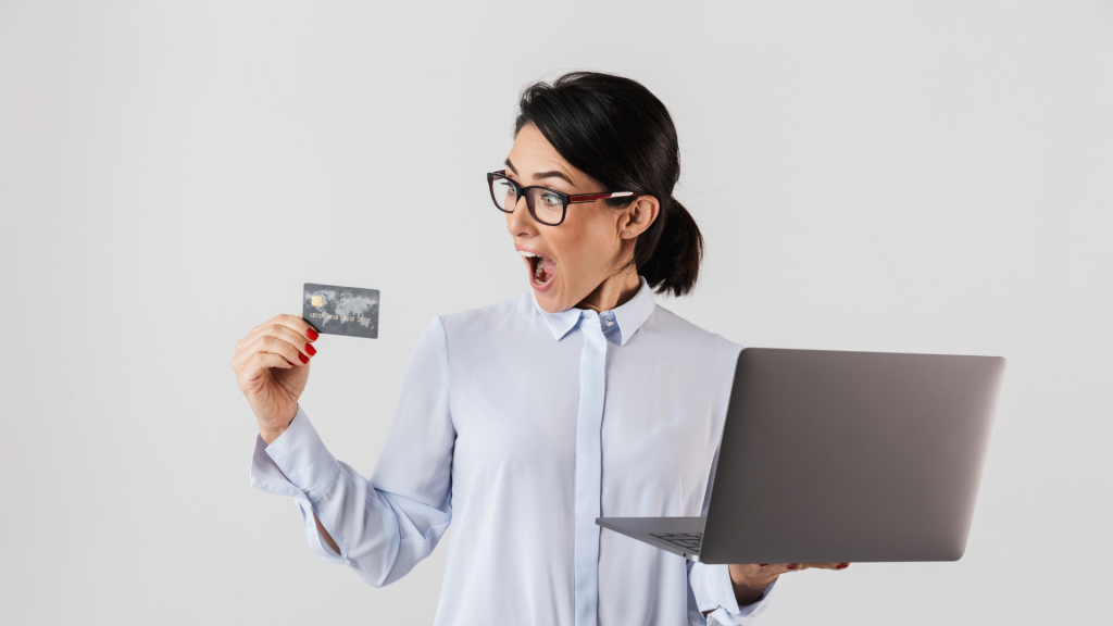 Portrait of confident businesswoman wearing eyeglasses holding silver laptop and credit card in the office, isolated over white background