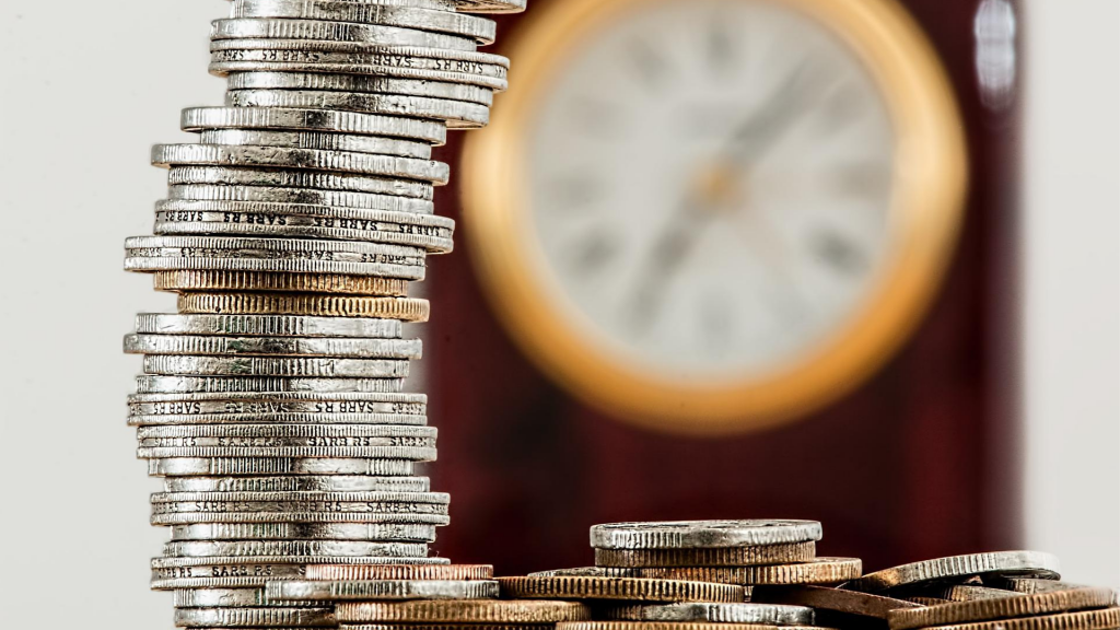 pile of money (coins) with blurred wall clock behind