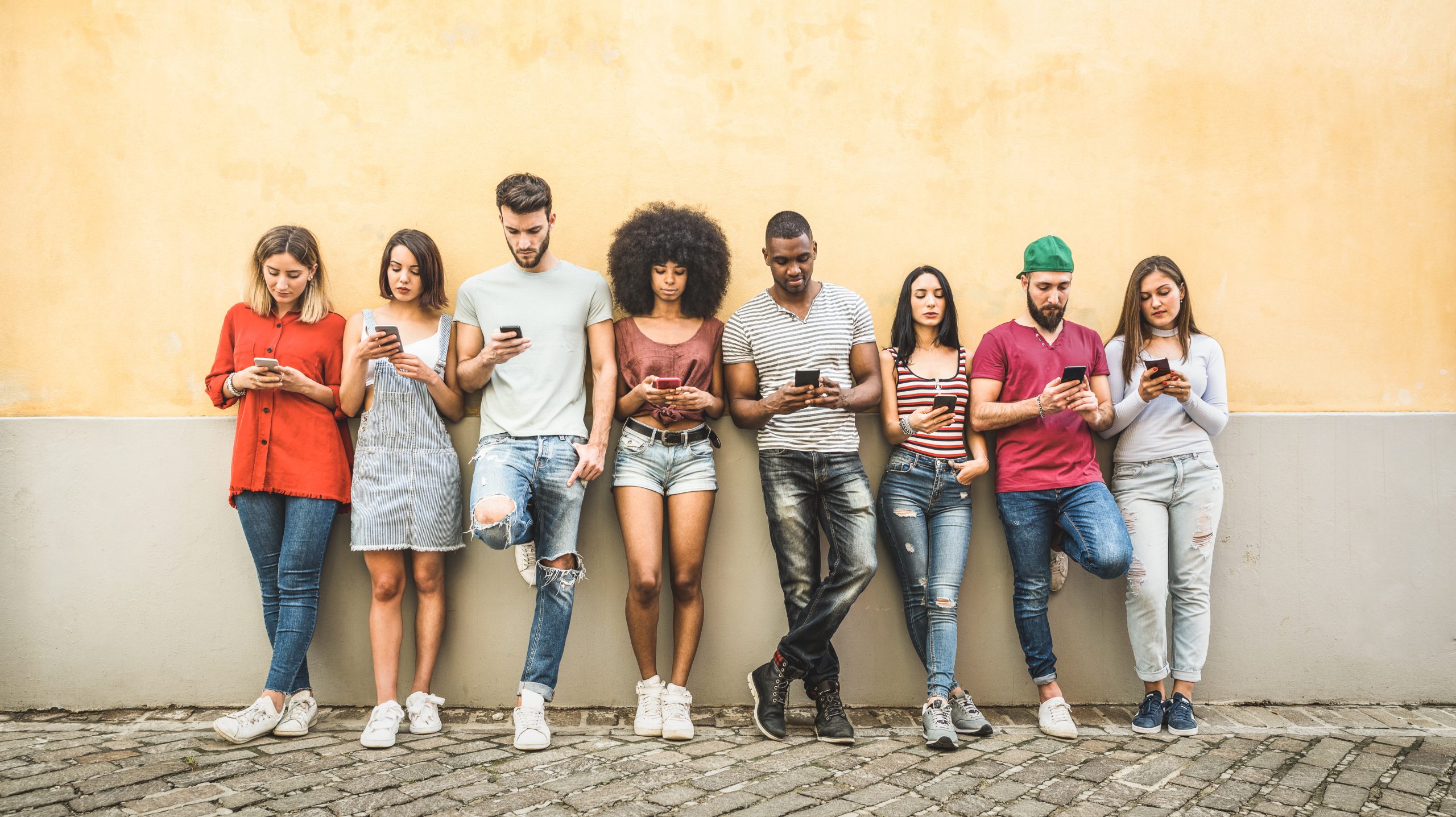 Multiracial friends using smartphone against wall at university