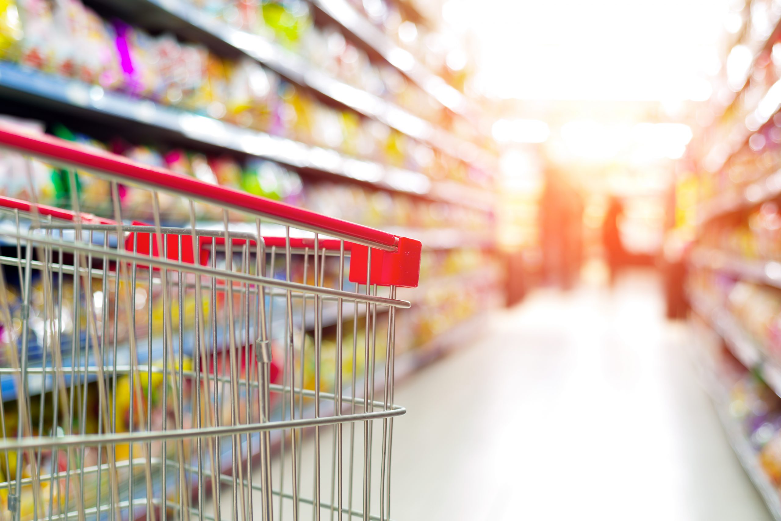 Supermarket interior, empty red shopping cart.