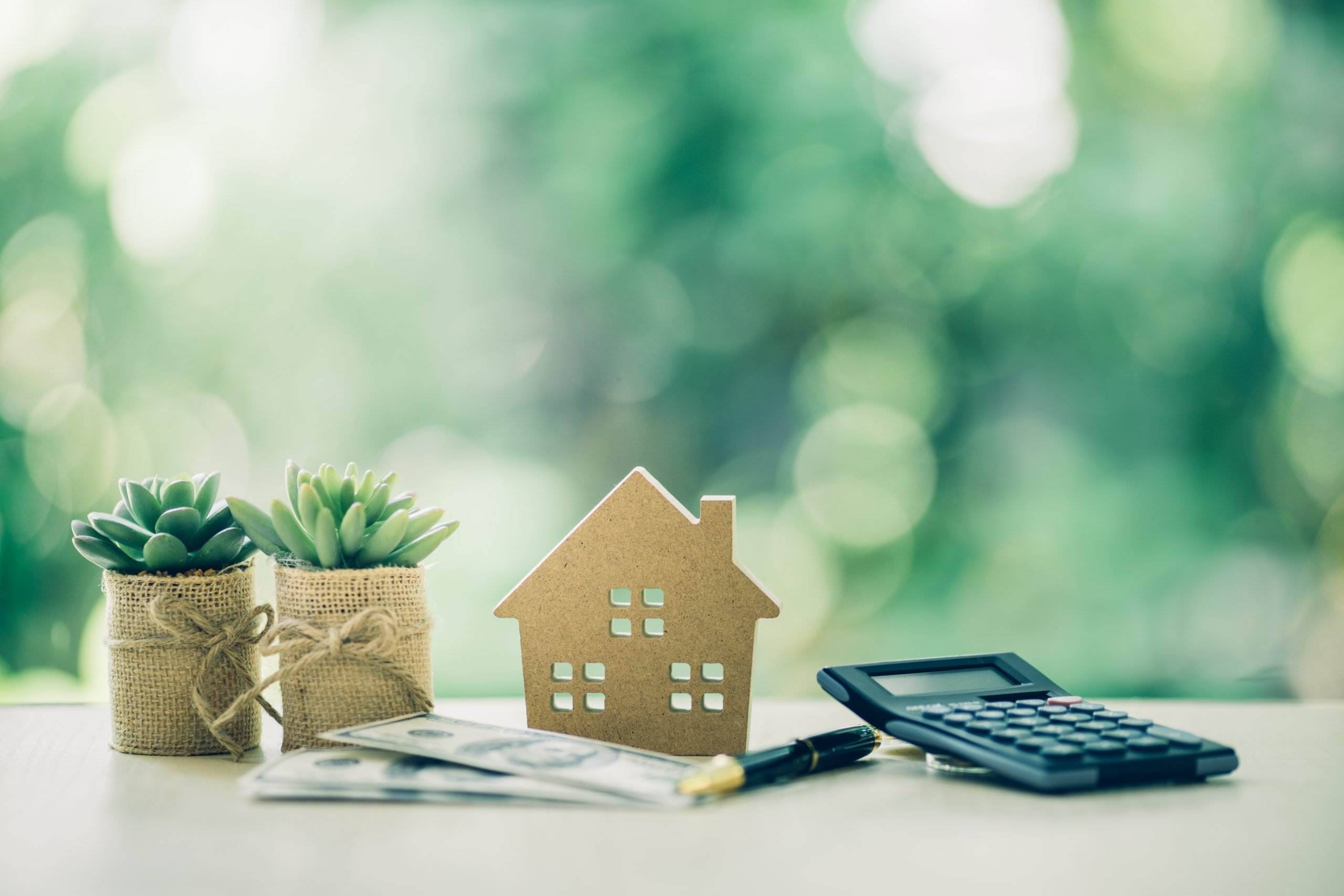 Wooden house, dollar bill and calculator on table