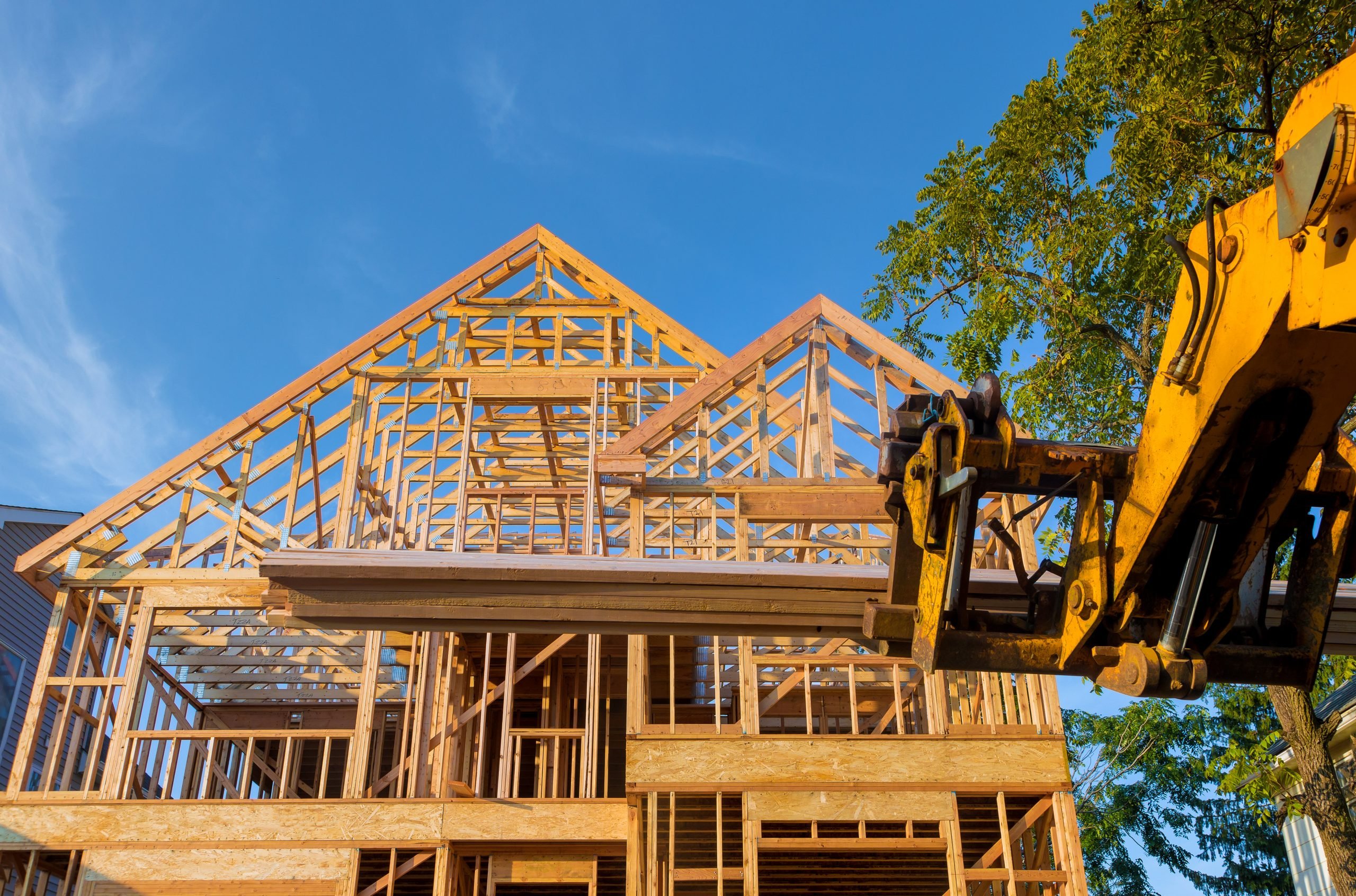 Heavy boom truck machinery is used to add the roof trusses to a timber frame house extension construction home framing