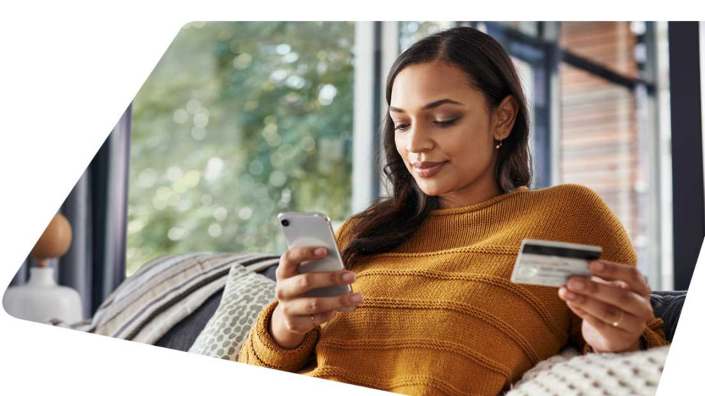 Woman using cellphone with white credit card in hand (apply Citi® Secured Mastercard®)