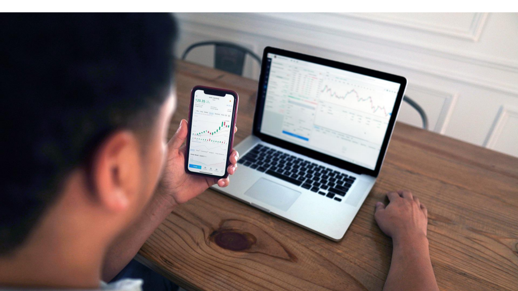 Man tracking financial market stocks on cellphone and notebook (investing for beginners).