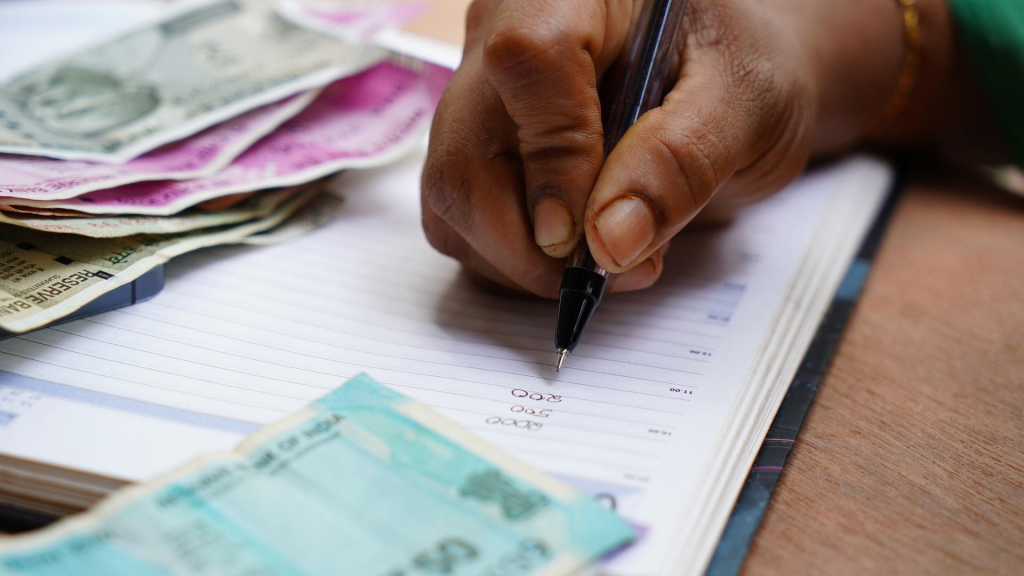 Person writing numbers in notebook around money, calculating (debt elimination plan)