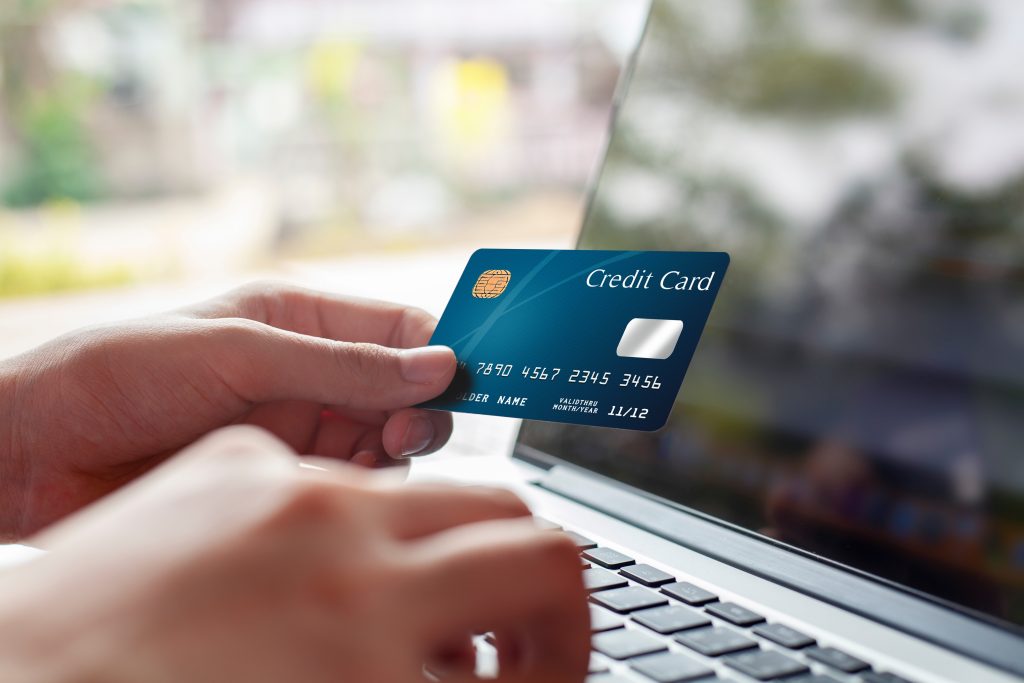 Woman hand holding blue credit card and using modern laptop, typ