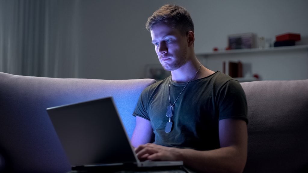 Serviceman searching job on laptop at home, adapting to civilian