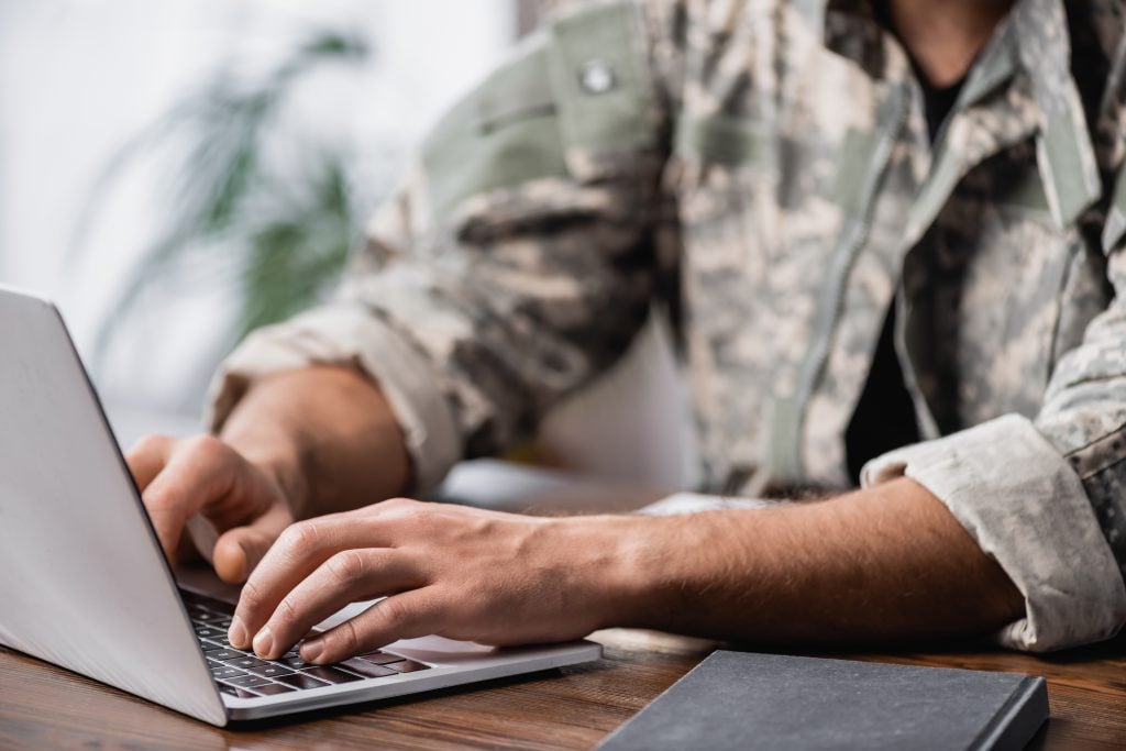 cropped view of military man using laptop on desk