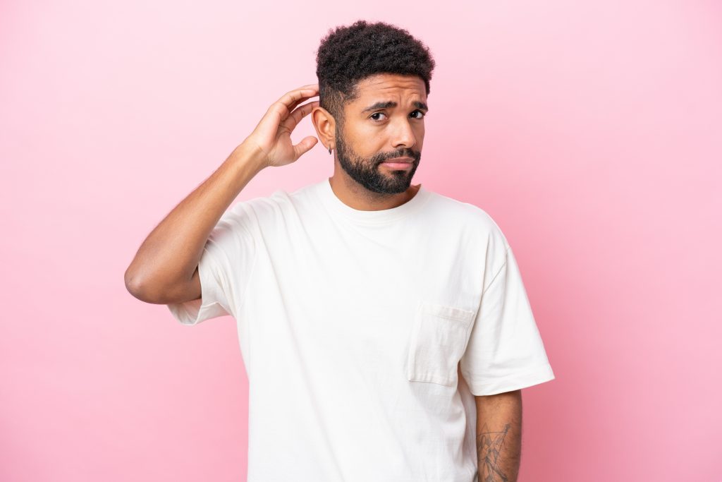 Young Brazilian man isolated on pink background having doubts