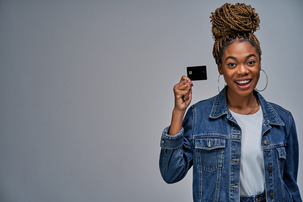 Happy lady with bun in a jeans jacket shows a black bank credit