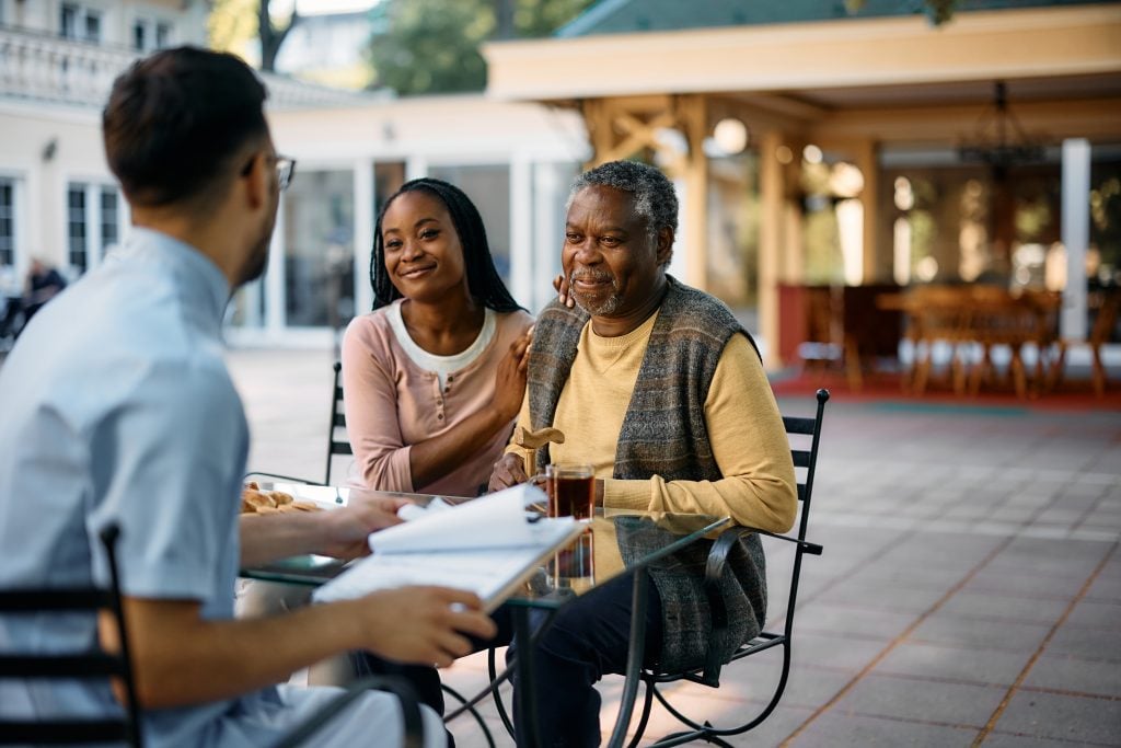 Happy black woman and her senior father talk to caregiver at nursing home.