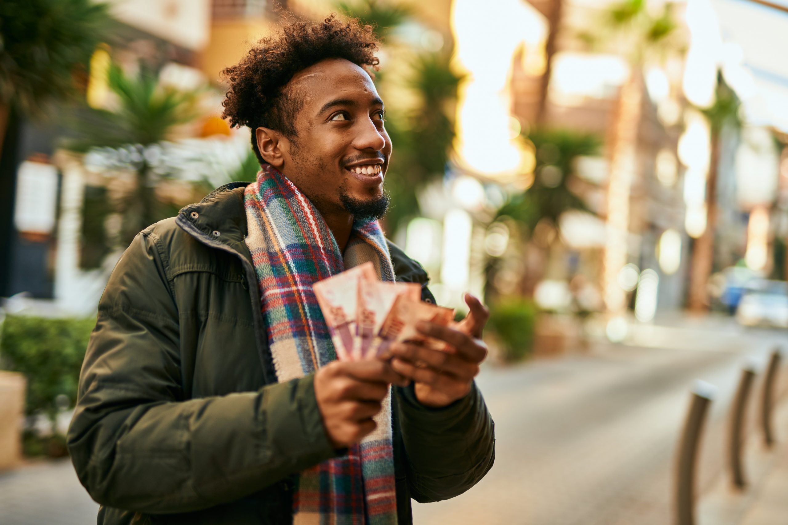 Young african american man smiling happy holding south africa rands banknotes at the city