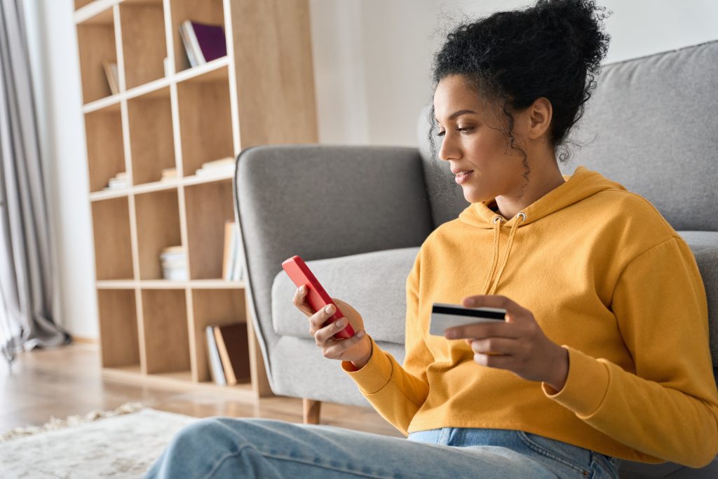 Young adult African american girl sitting indoors doing mobile payment online.