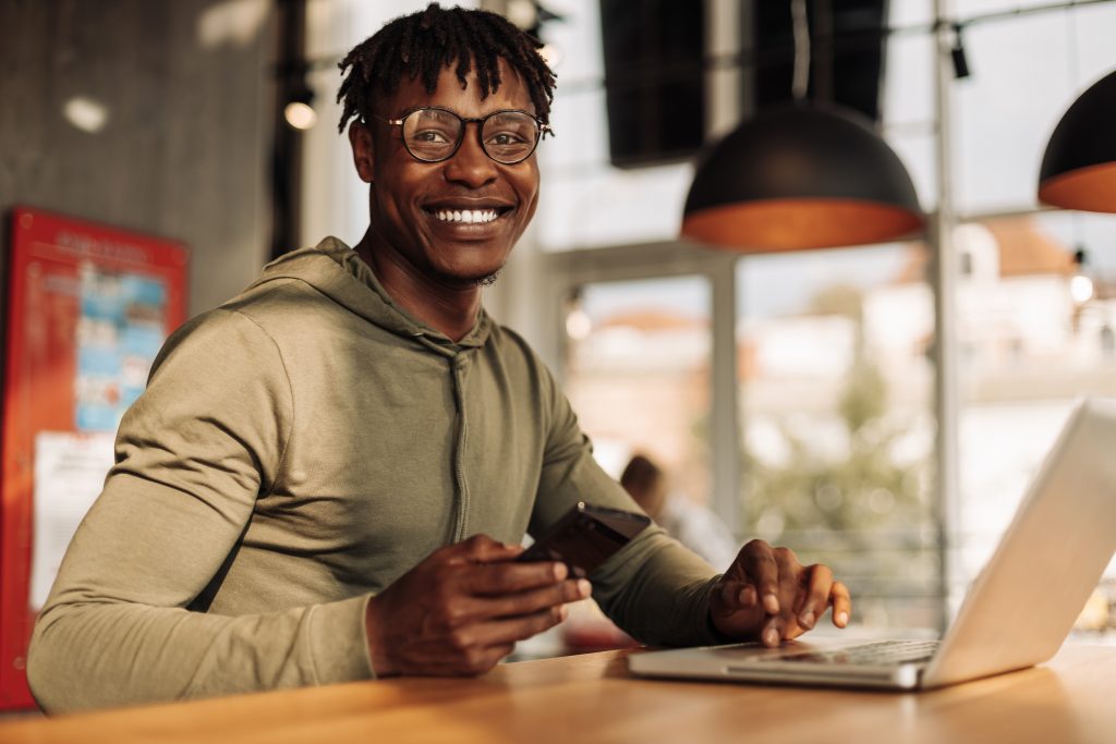 African American man with a laptop and a phone in his hands, sitting at a table in the office. work online