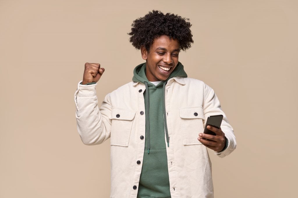 Happy African American teenager using cell phone looking at mobile.
