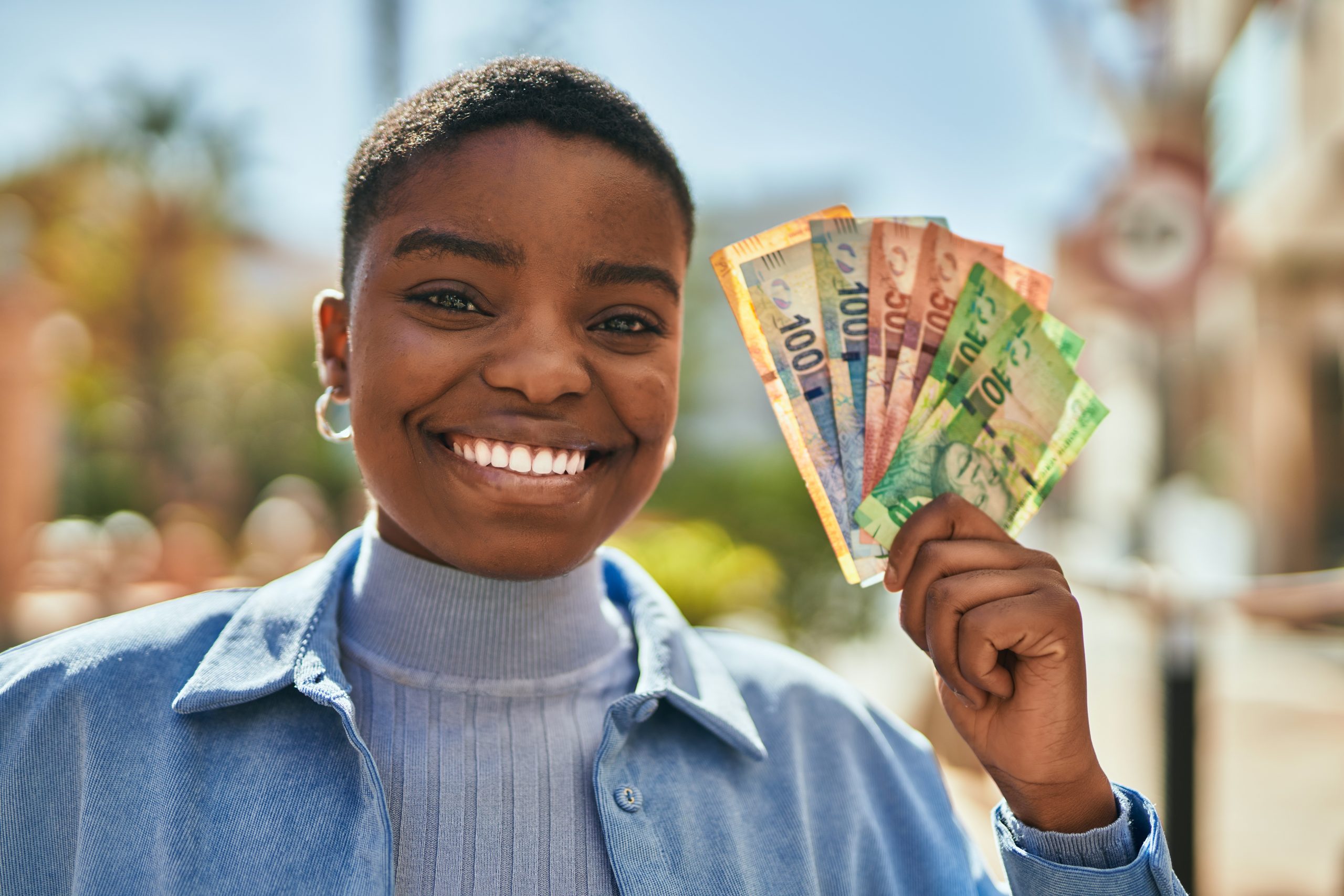 Young african american woman smiling happy holding south africa rand banknotes at the city.