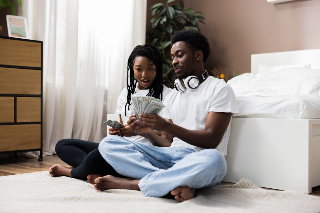 Happy african american young couple calculating counting domestic rate bank loan payment at home, smiling interracial family planning budget manage household expenses paperwork