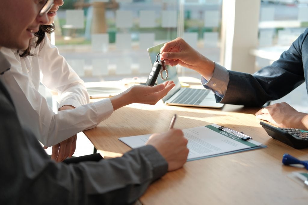 dealer salesman giving car key to owner. client signing insuranc