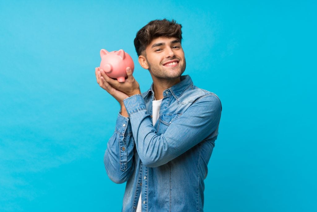 Young handsome man over isolated blue background holding a big piggybank