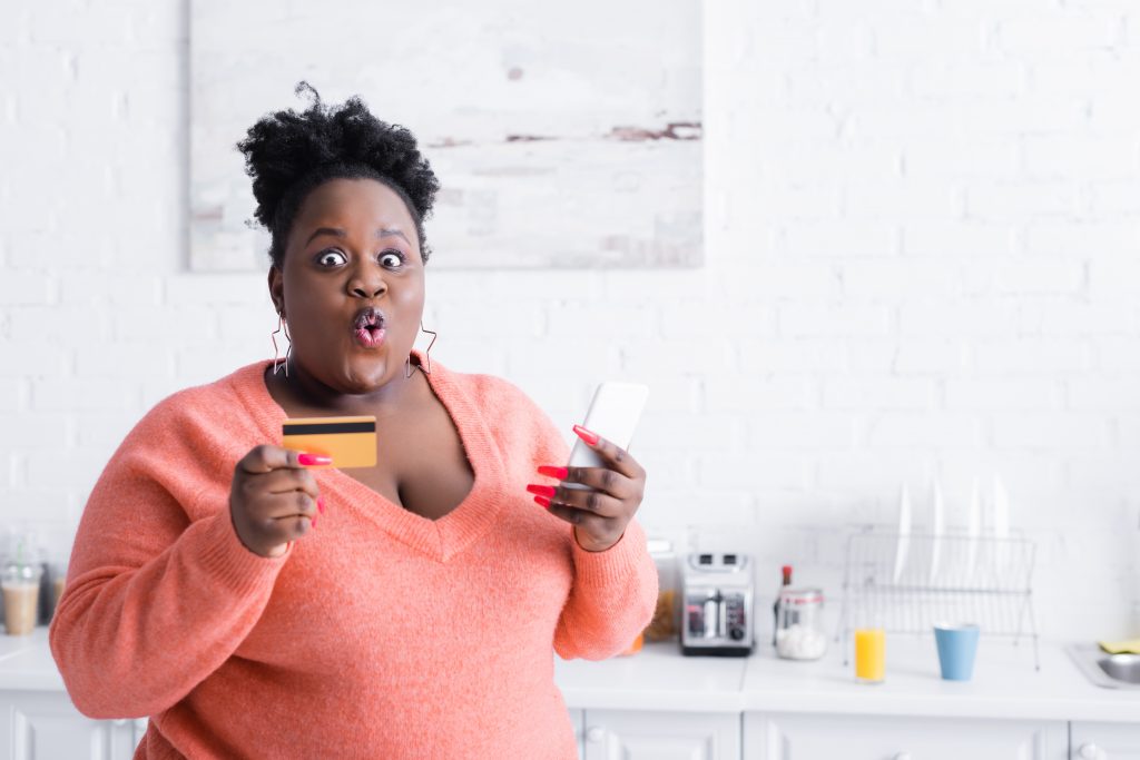 shocked african american plus size woman holding credit card and