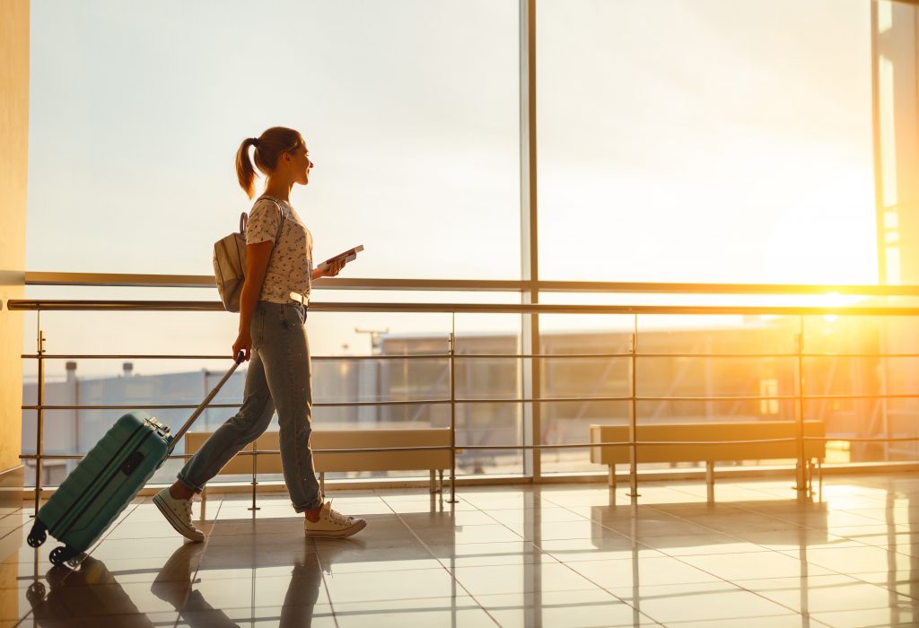 young woman goes at airport at window with suitcase waiting for plane