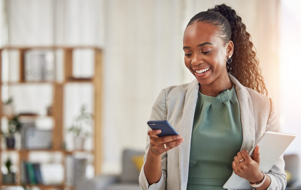 Happy black woman, phone and communication at office with smile in networking or social media. African female person or employee enjoying online browsing or chat on mobile smartphone app at workplace