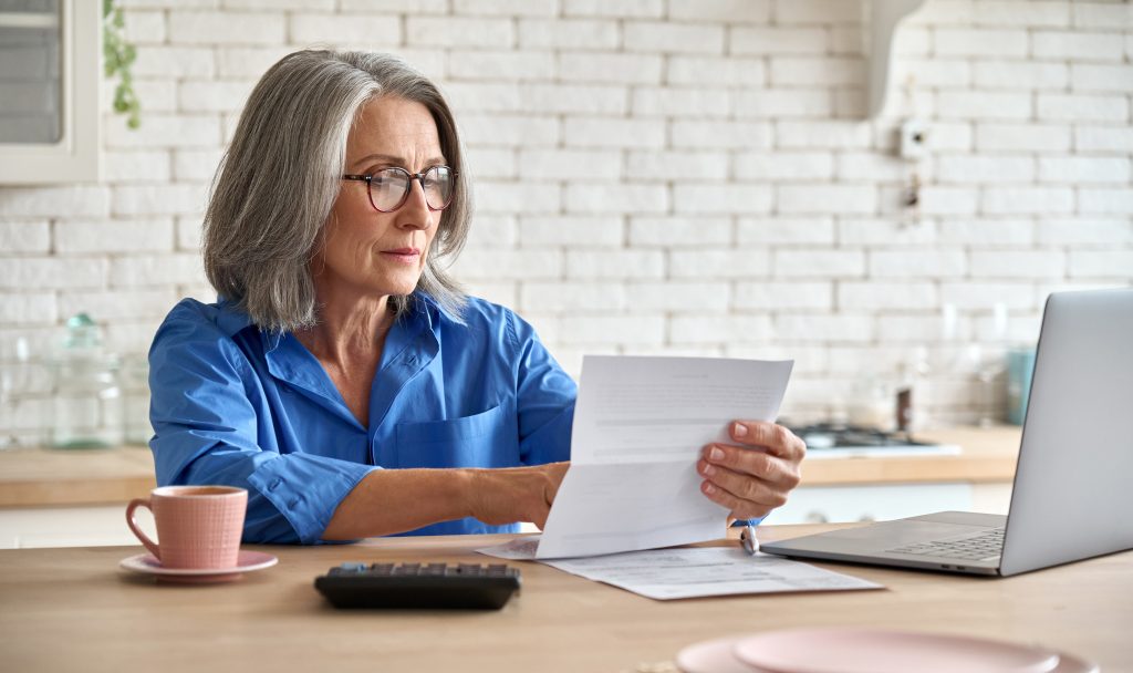 Senior mid 60s aged woman calculating bank fee with computer.