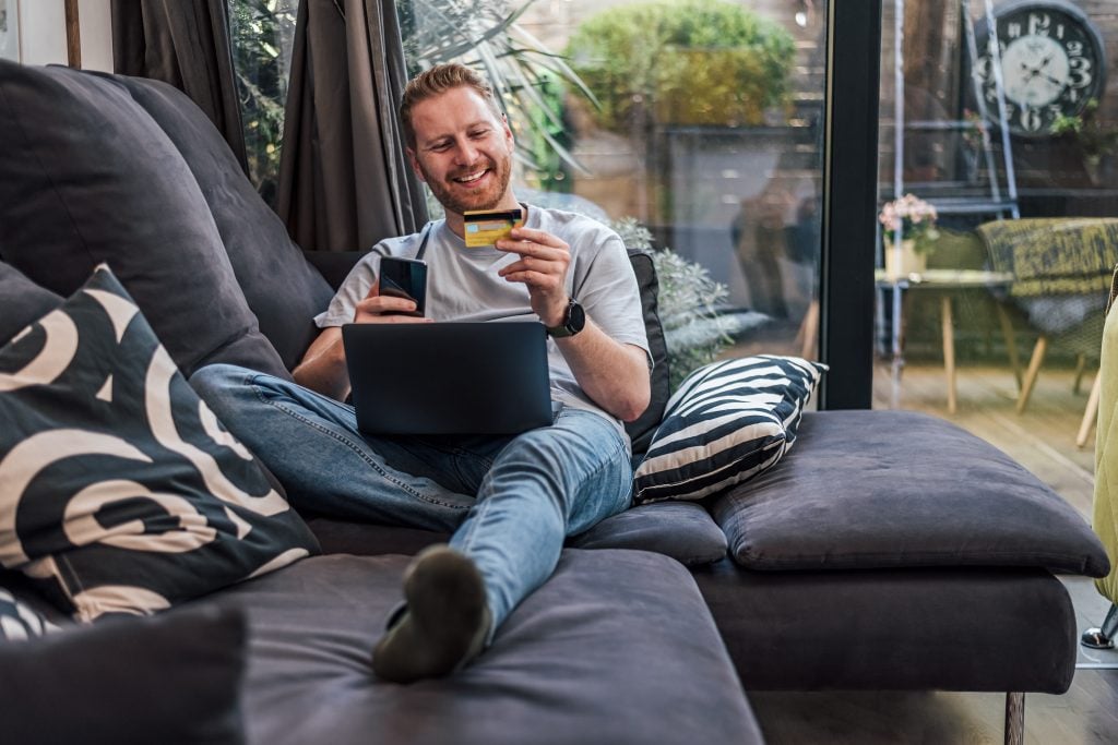 Smiling caucasian man, using his credit card and laptop, at home.