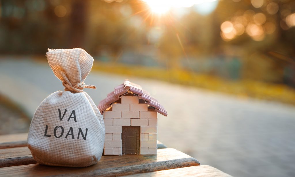 Va loan concept - government-backed mortgage option available to Veterans, service members and surviving spouses. Money bag and miniature house in the park in the sunset light. Real estate and finance